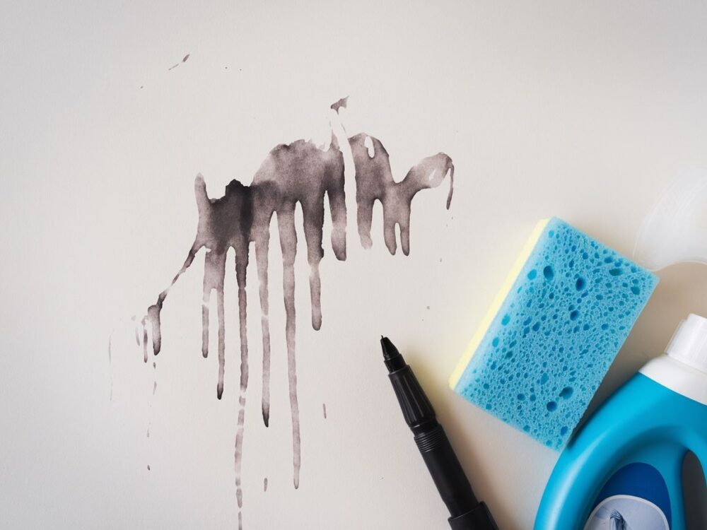 Ręka trzymająca gąbkę przy ścianie z plamą atramentu